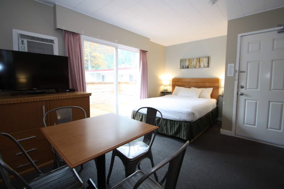A hotel room with a bed, a desk with a chair, a television, and a window with curtains.