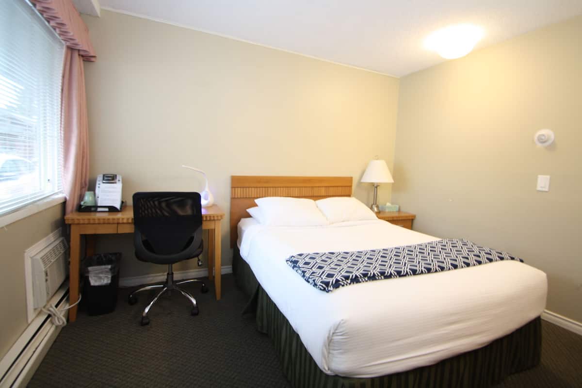 A hotel room with a bed, a desk, a chair, and a window with curtains.