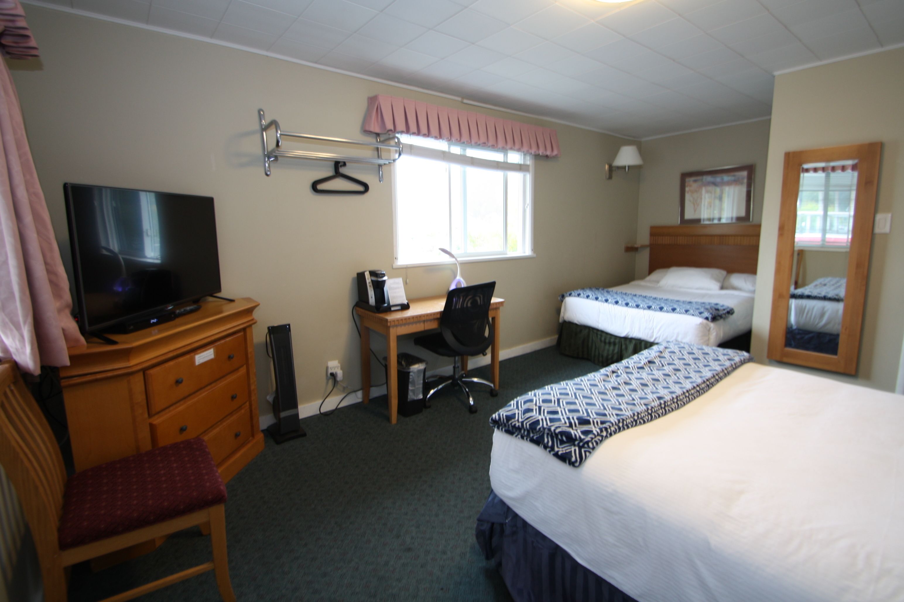 A hotel room with a bed, a desk with a chair, a television, a window with a curtain, and a mirror.