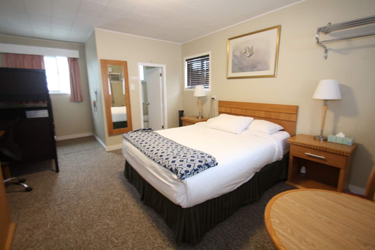 A hotel room with a bed, bedside tables, a desk, a chair, a window with blinds, and a framed picture on the wall.