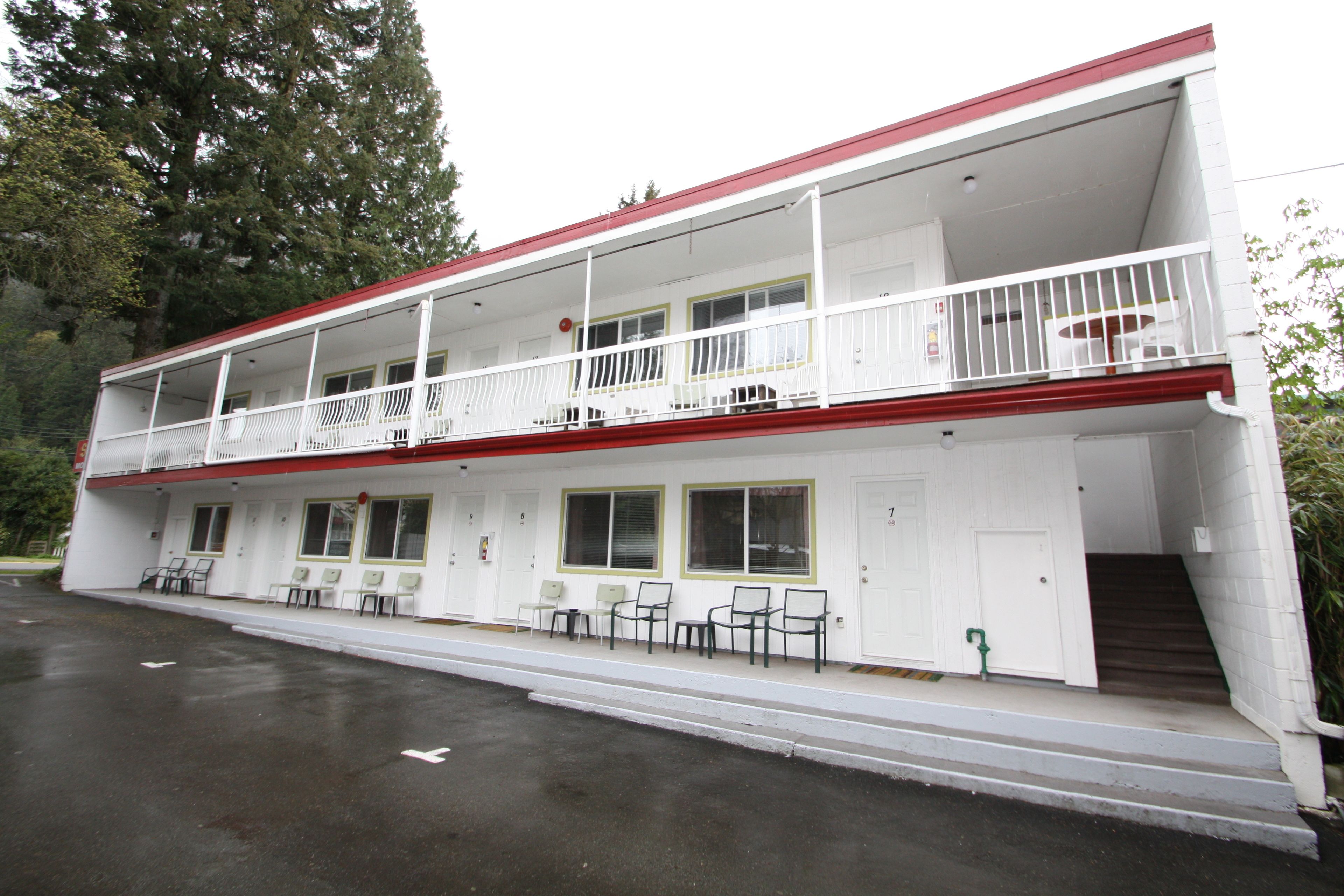 A two-story building with a red roof, white exterior, and a balcony on the upper floor. There are several chairs and tables outside on the ground floor.