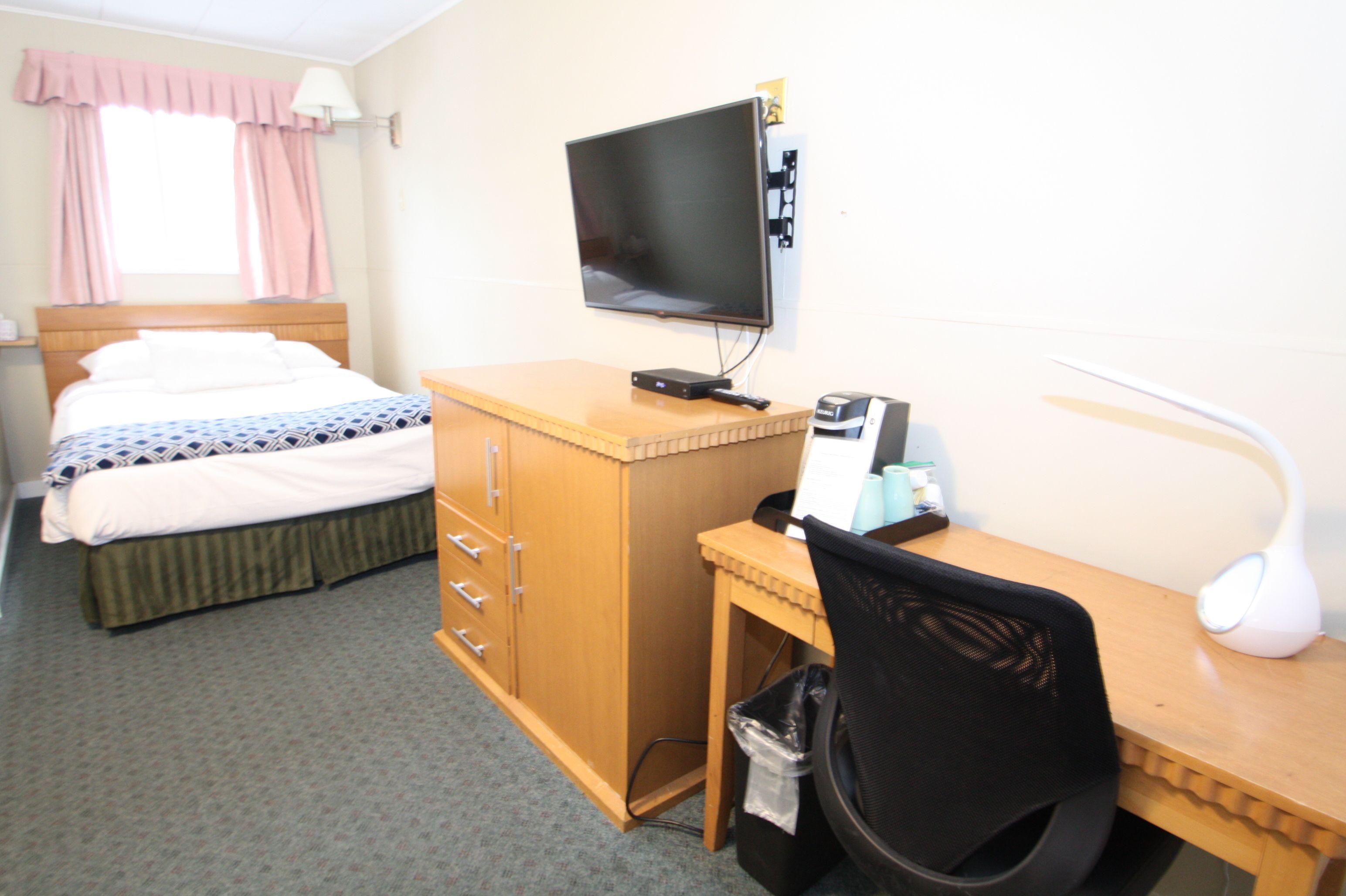 A hotel room with a bed, a desk with a computer, a TV, and a lamp.