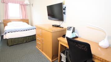 A hotel room with a bed, a desk with a computer, a TV, and a lamp.