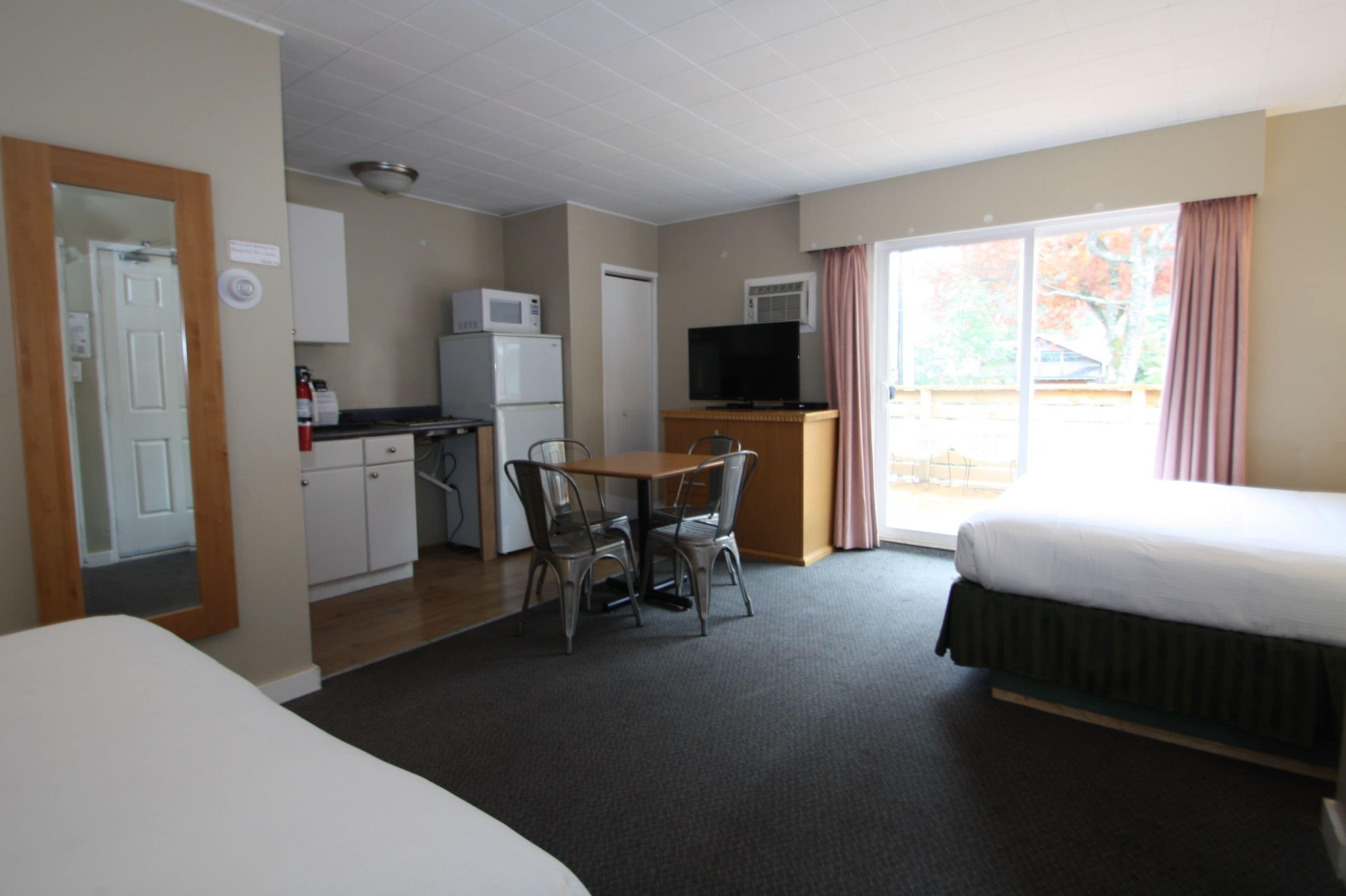 Habitación de hotel con una cama, un escritorio con silla, un microondas, un televisor y una ventana con cortinas.