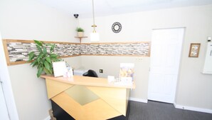 A reception desk with a plant, a clock, and a door in the background. - Harrison Spa Motel (Harrison Hot Springs)
