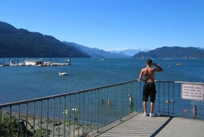 A wooden dock with a metal railing overlooking a lake with boats and mountains in the background.