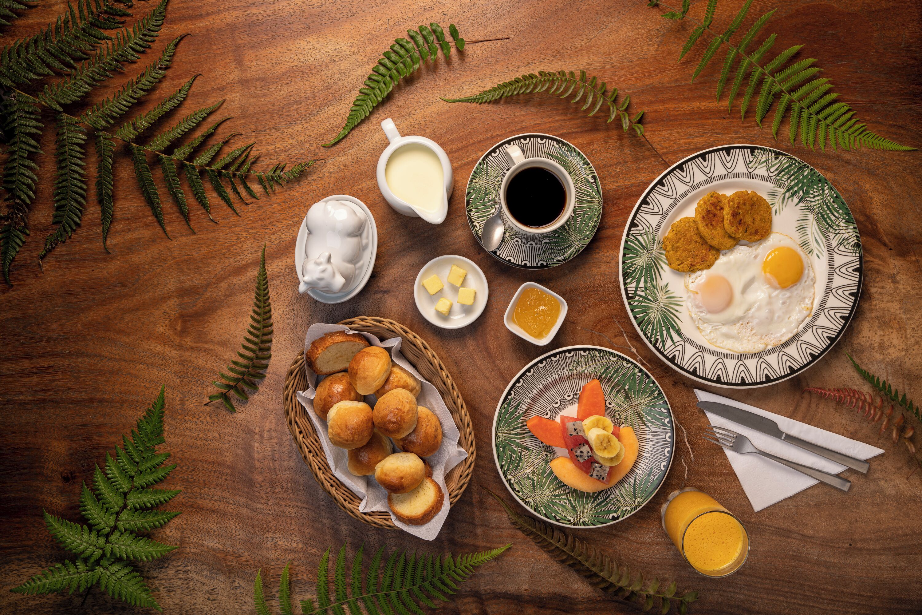 A breakfast table with various food items, a cup of coffee, and a basket of rolls.