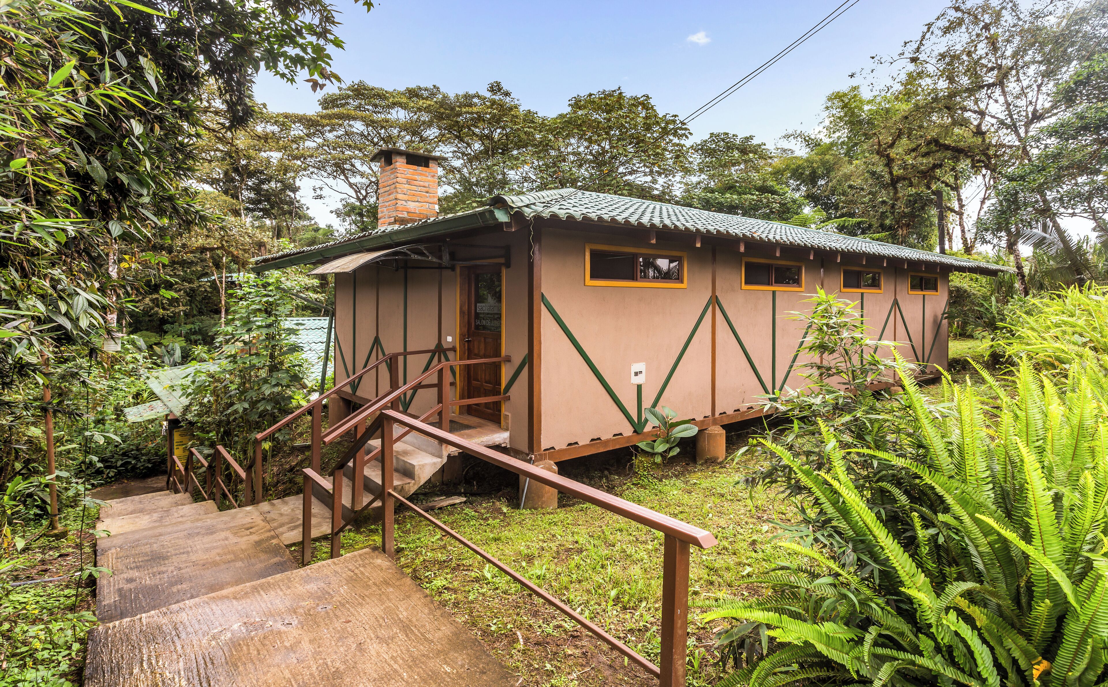 A small, single-story building with a staircase leading to a door, surrounded by dense greenery.