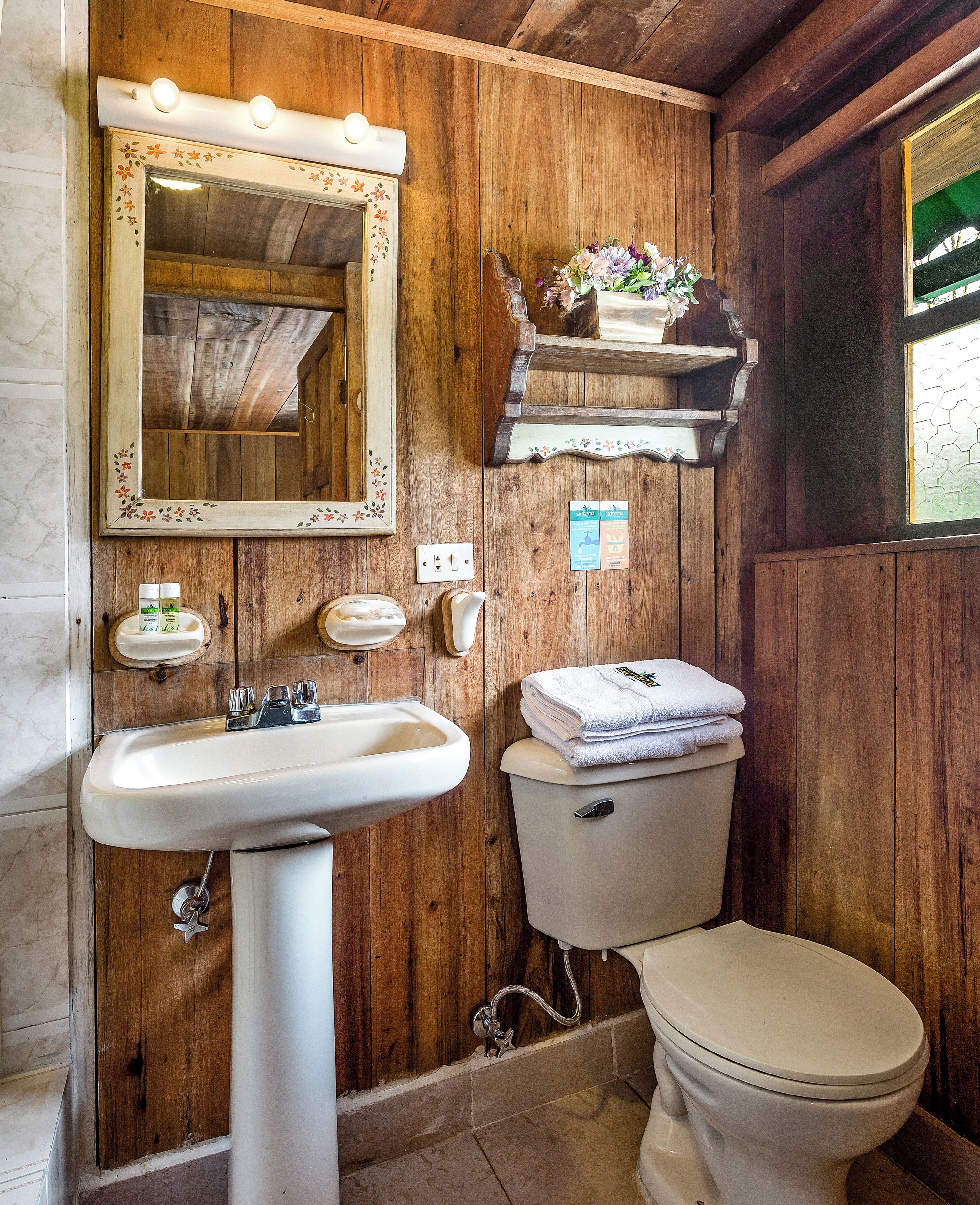 Une salle de bain en bois avec un lavabo, un miroir et des toilettes, le tout de couleur blanche.