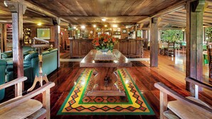 A wooden interior with a central table, green sofas, and a patterned rug. - Sachatamia Lodge (Mindo)