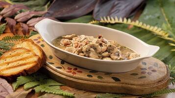 A bowl of mushroom soup on a wooden board with decorative leaves, accompanied by a slice of toasted bread.