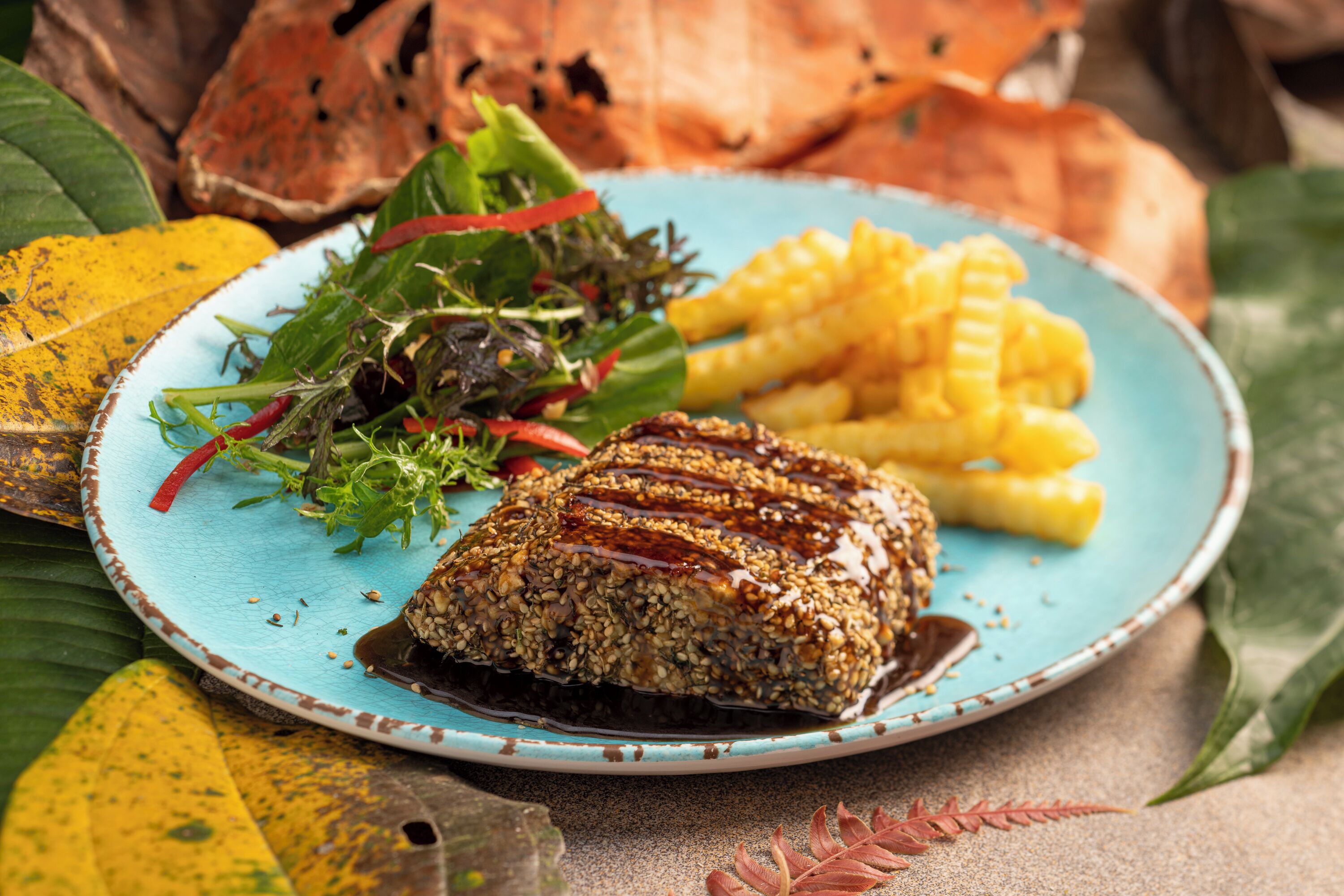 Une assiette contenant une viande grillée, garnie de graines et de sauce, accompagnée d’une salade et de frites.