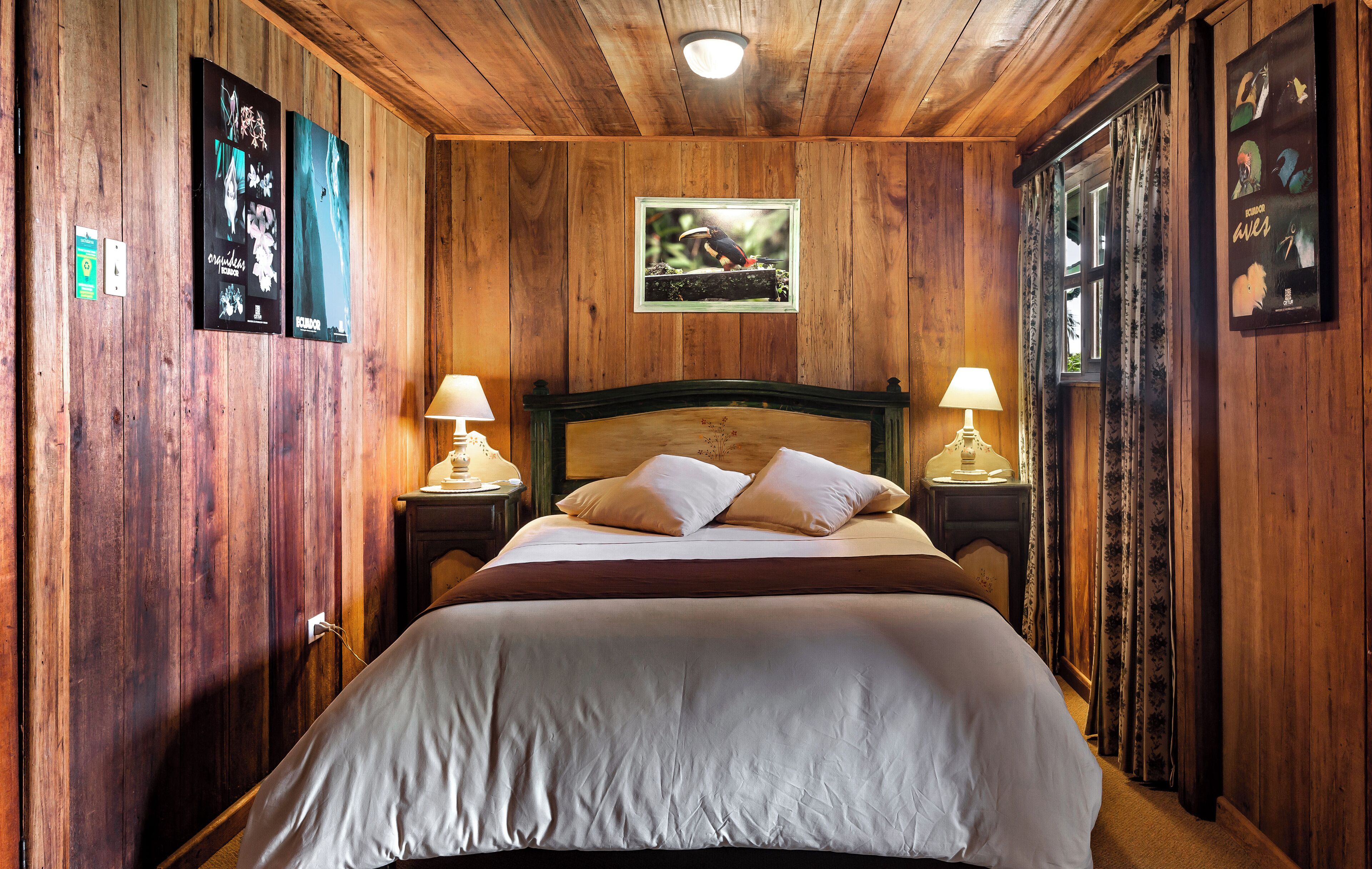 Una habitación con paneles de madera, una cama grande, dos lámparas de noche y cuadros en las paredes.