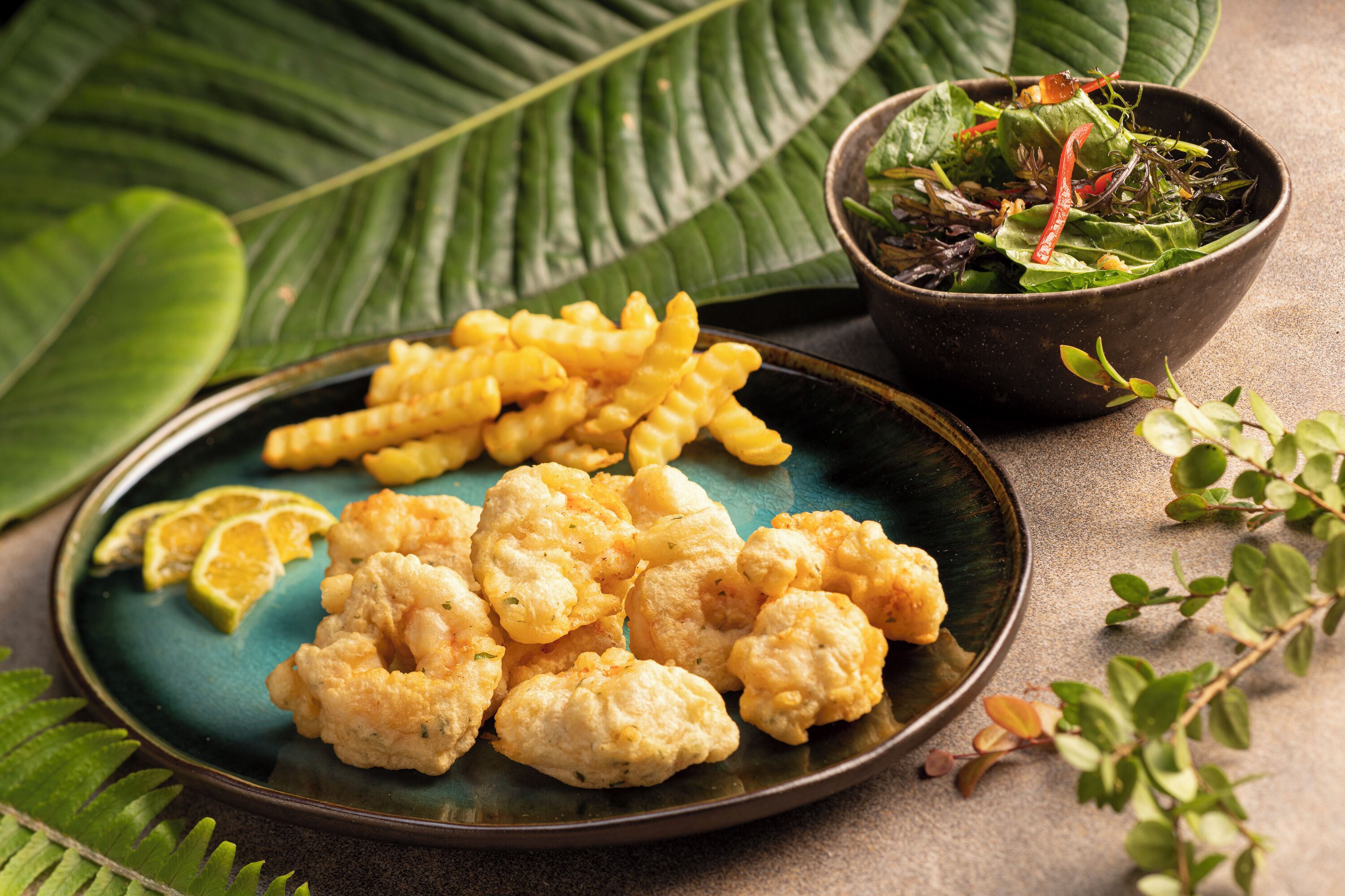 A plate of fried cauliflower and fries with a side salad on a table.