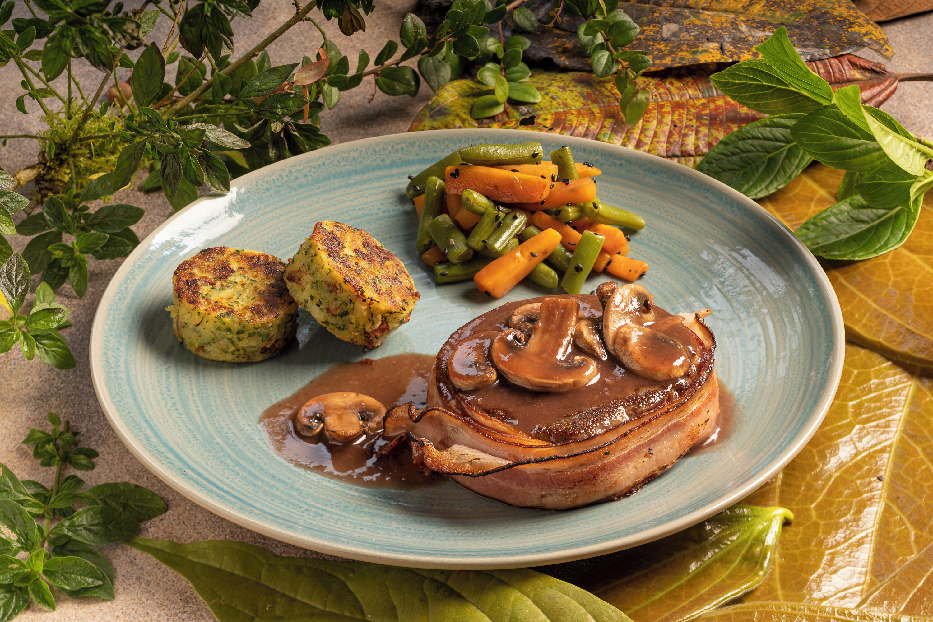 A plate with a pork chop, green beans, carrots, and two potato patties.