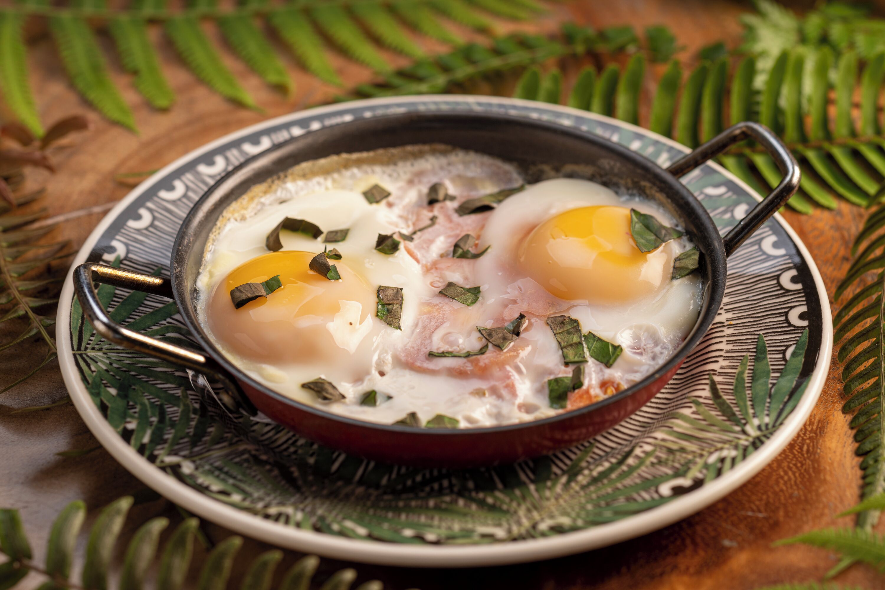 Un bol con huevos, hierbas y jamón sobre un plato estampado.