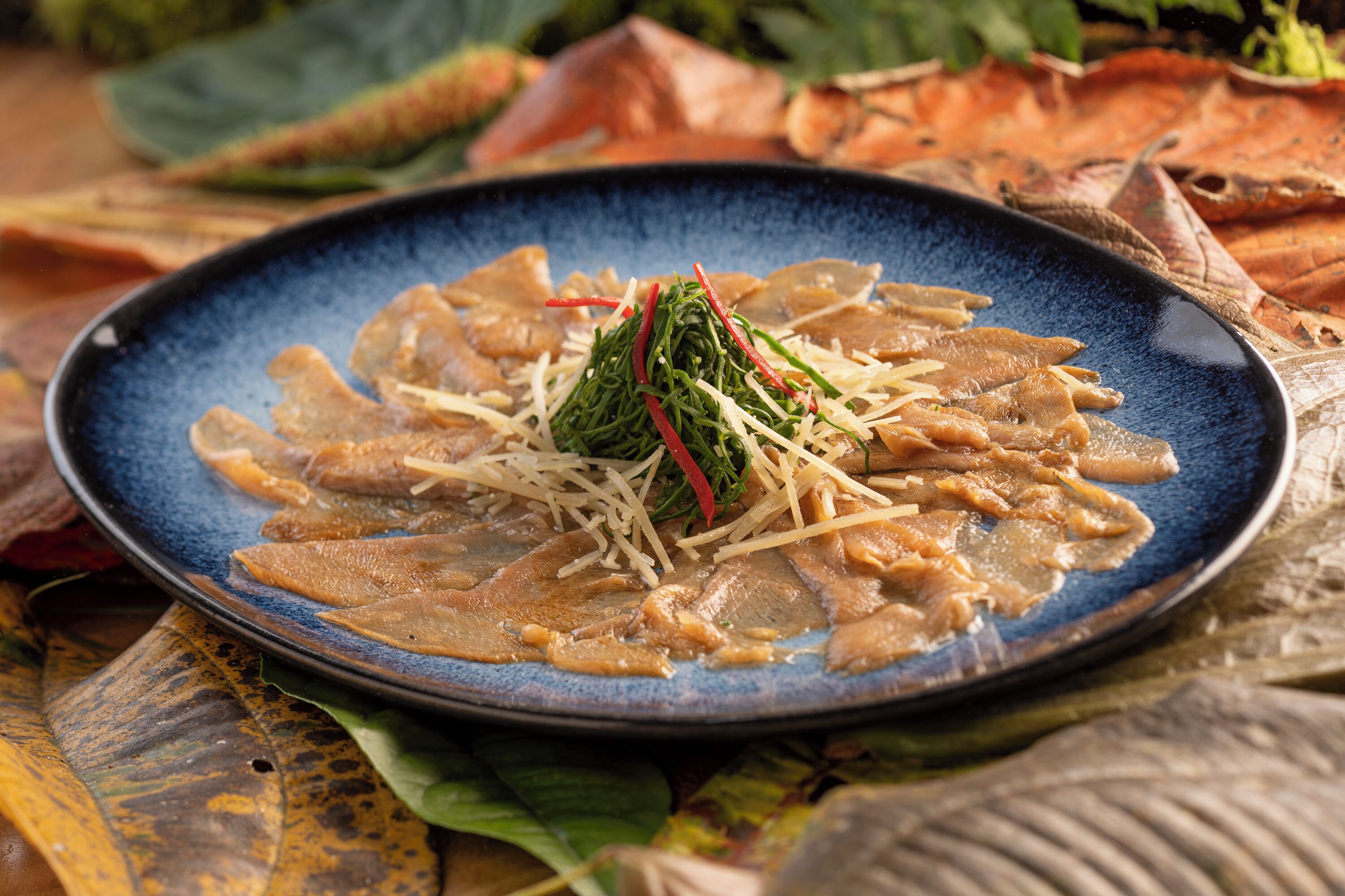 A blue plate with sliced meat and shredded vegetables on a table with autumn leaves.