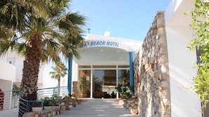 A hotel entrance with a stone facade, palm trees, and a clear sky. - Irina Beach Hotel (Kos)