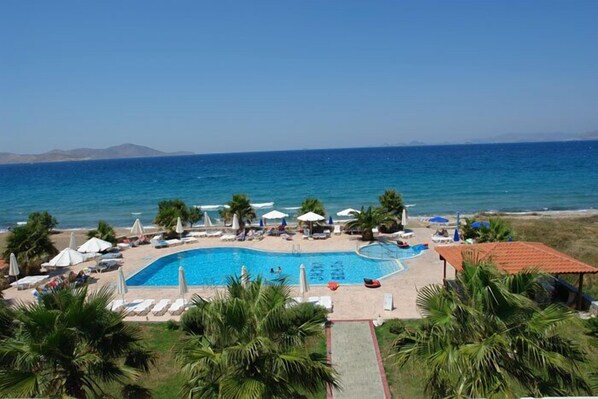 Ein Poolbereich mit Liegestühlen und Sonnenschirmen, umgeben von Palmen und Blick auf das Meer.