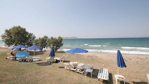 A beach with sun loungers and umbrellas, a clear sky, and the ocean in the background. - Irina Beach Hotel (Kos)