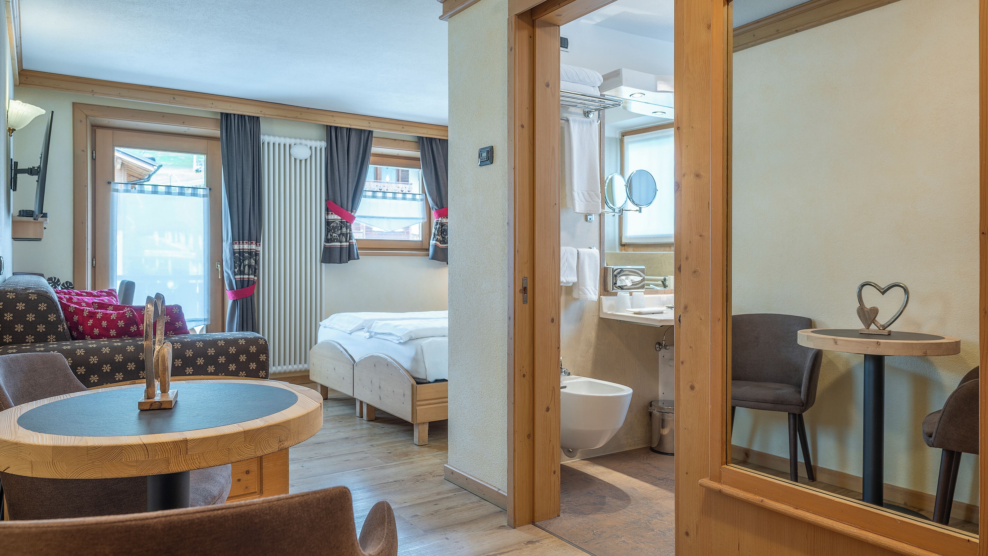 A cozy room with a bed, a round wooden table, and a small bathroom.