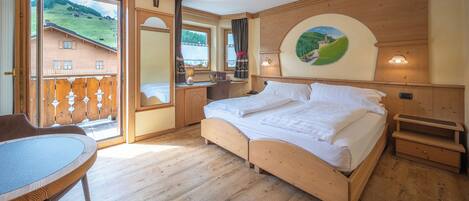 Un dormitorio con cama de madera, un escritorio y una silla. Hay un balcón con vistas a una casa y árboles.
