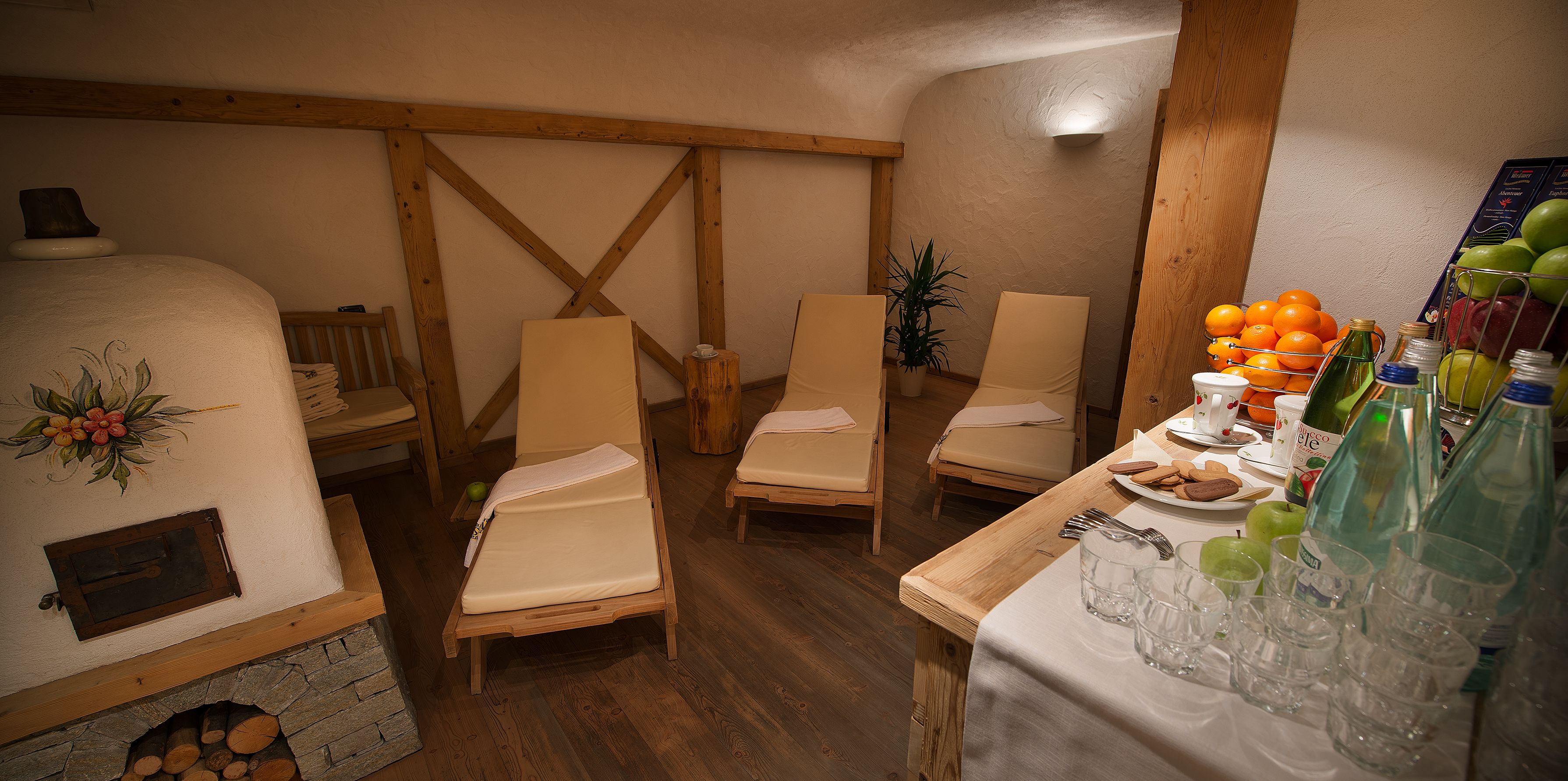 A cozy room with a fireplace, wooden beams, and a table set with glasses, fruits, and bottles.