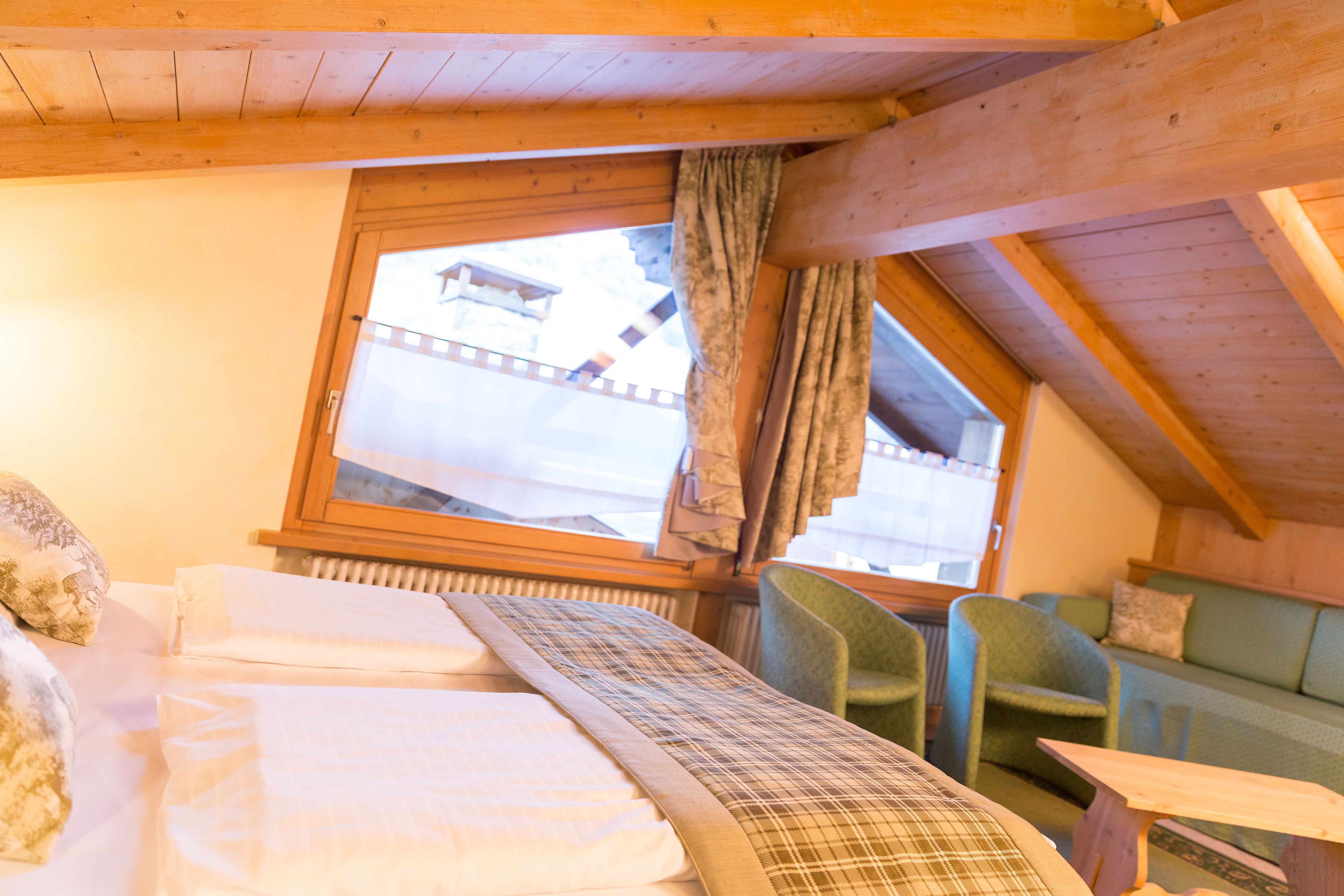 Una habitación acogedora con una cama, una ventana con cortinas, un sillón verde y una mesa de madera.