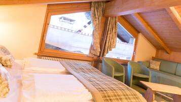 Una habitación acogedora con una cama, una ventana con cortinas, un sillón verde y una mesa de madera.