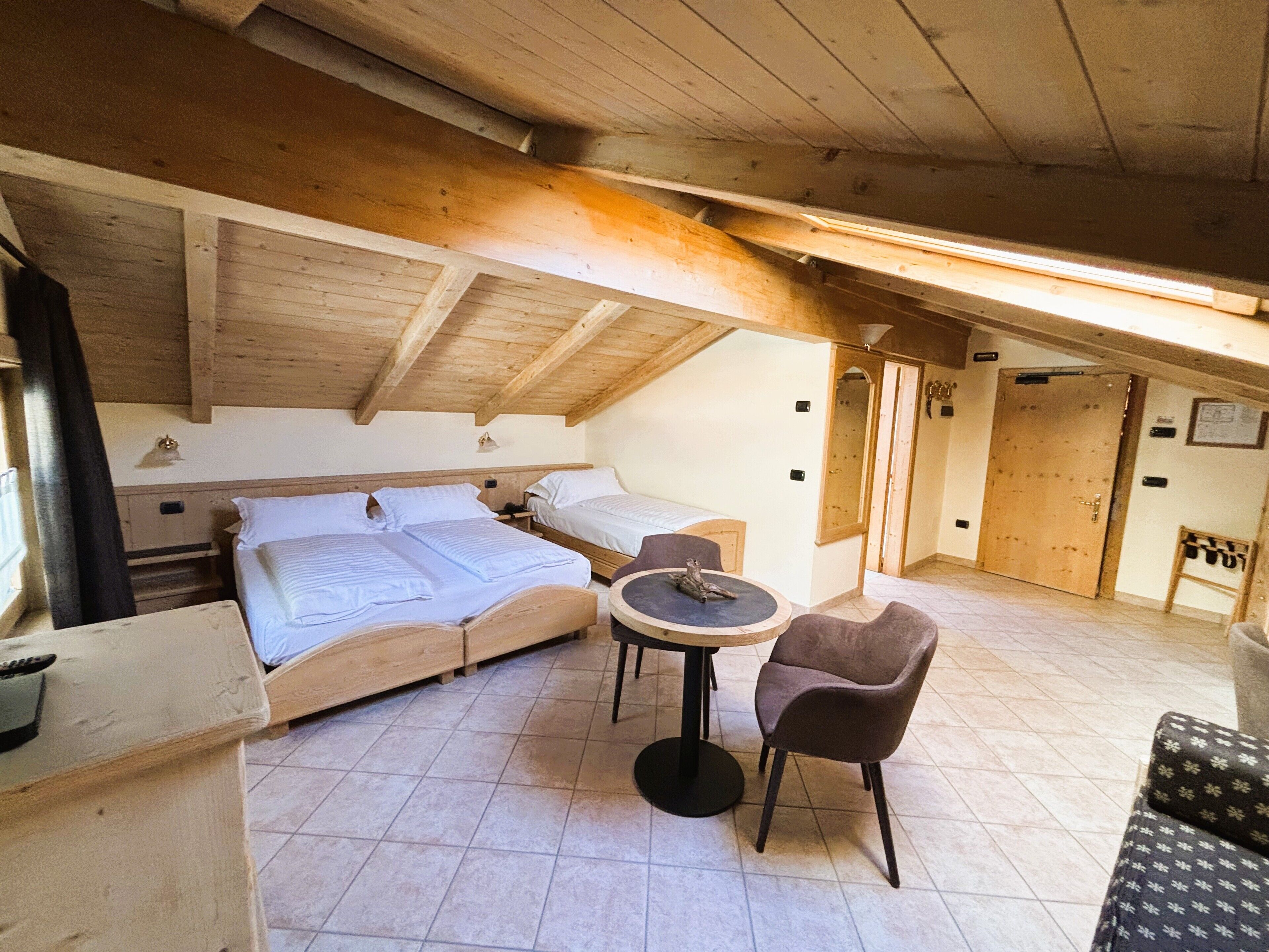 A cozy attic bedroom with two beds, a round table, and a chair.