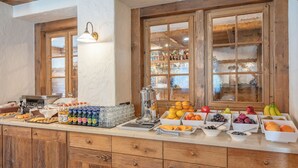 A buffet setup with various food items and beverages, wooden cabinets, and a window with a view of a snowy landscape. - Hotel Crosal (Livigno)