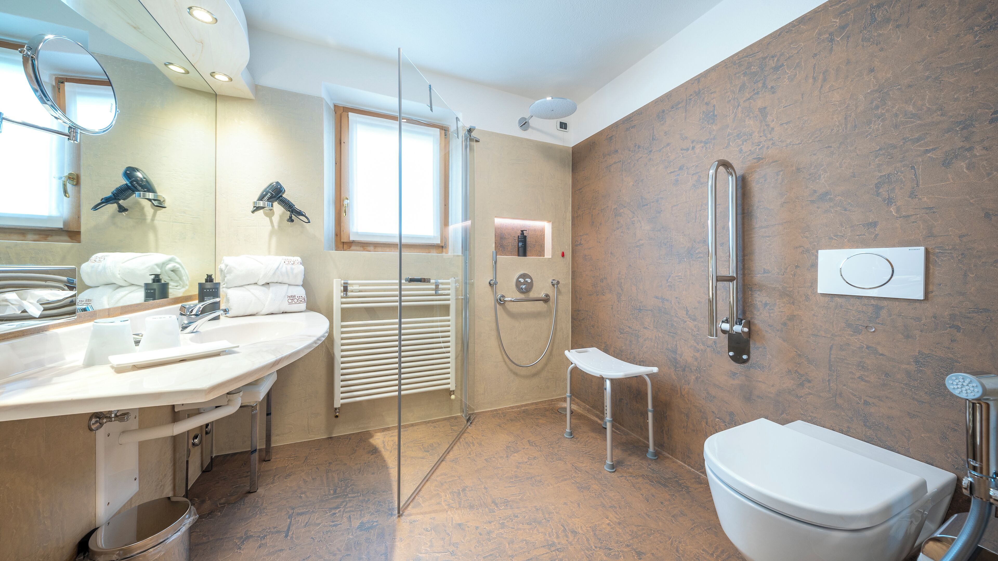 A modern bathroom with a large mirror, a sink with toiletries, a shower with a handheld showerhead, and a toilet.