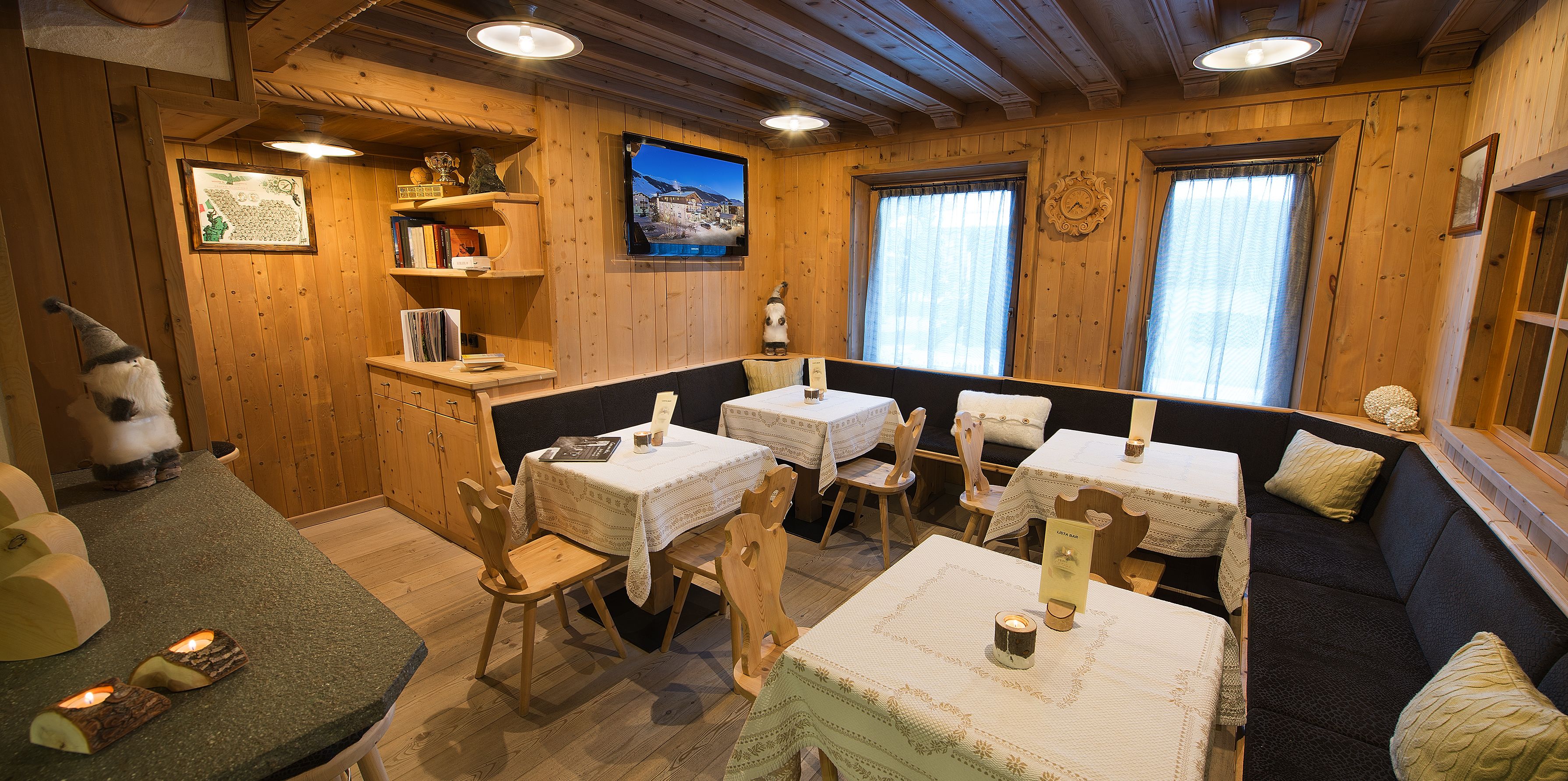 A cozy cabin interior with wooden walls, a television mounted on the wall, and a seating area with tables and chairs.