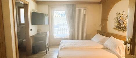 Una habitación de hotel con una cama, un escritorio con silla, un televisor y una ventana con cortinas.
