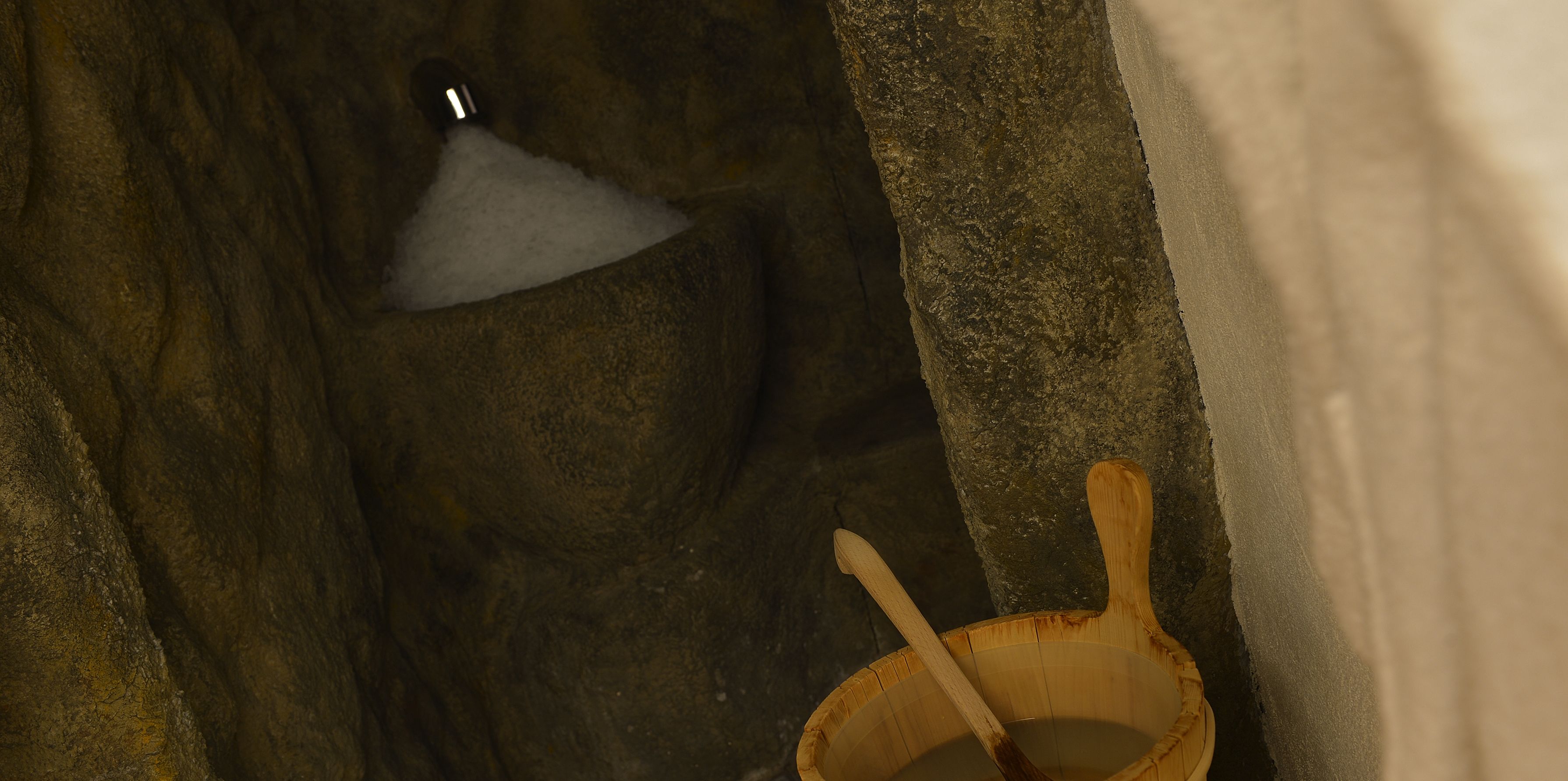 A stone basin with a wooden ladle, a stone wall, and a small wooden bucket.