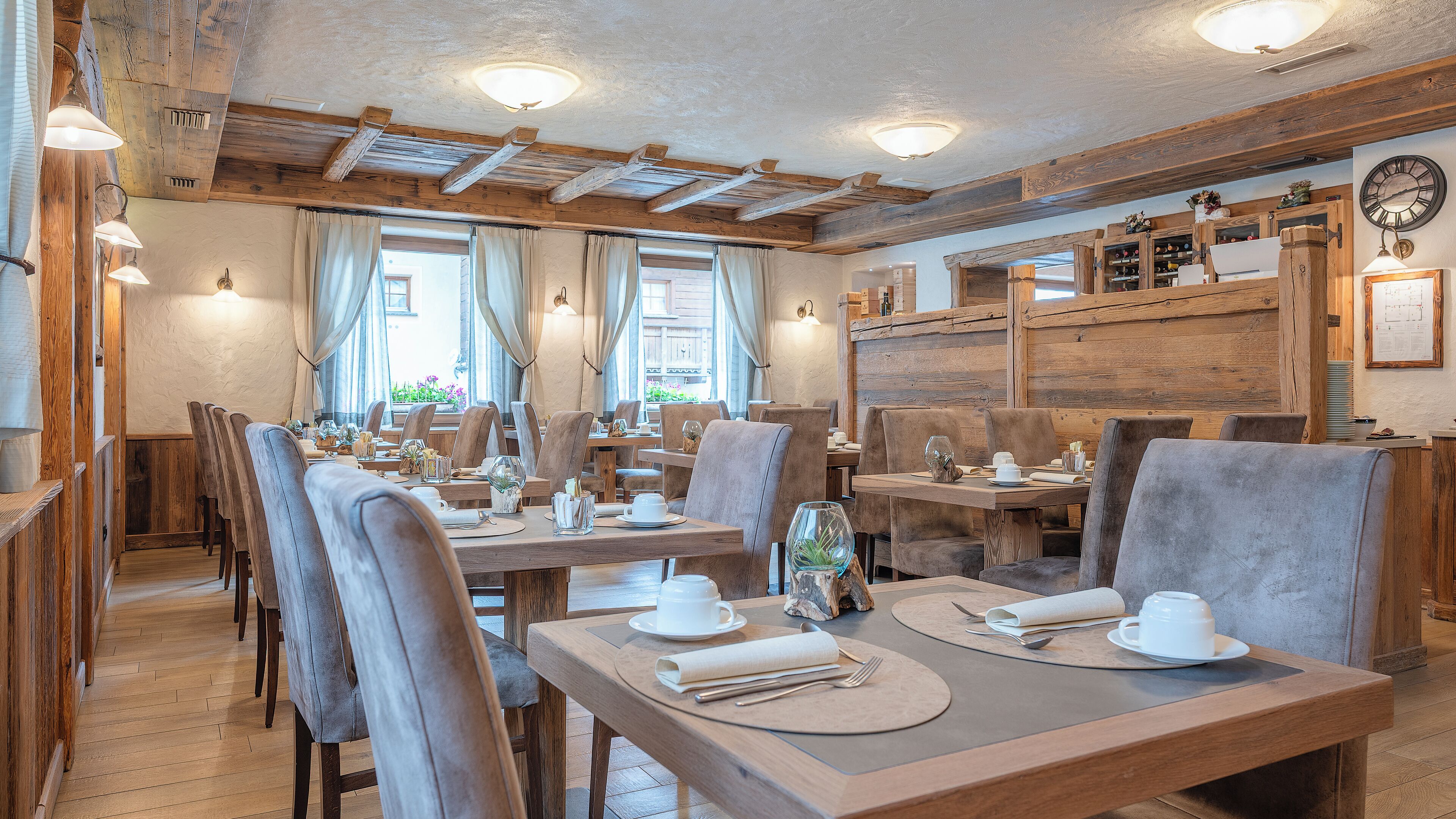 Ein Restaurant mit Holztischen und -stühlen, einer Wanduhr und einem Fenster mit Vorhängen.