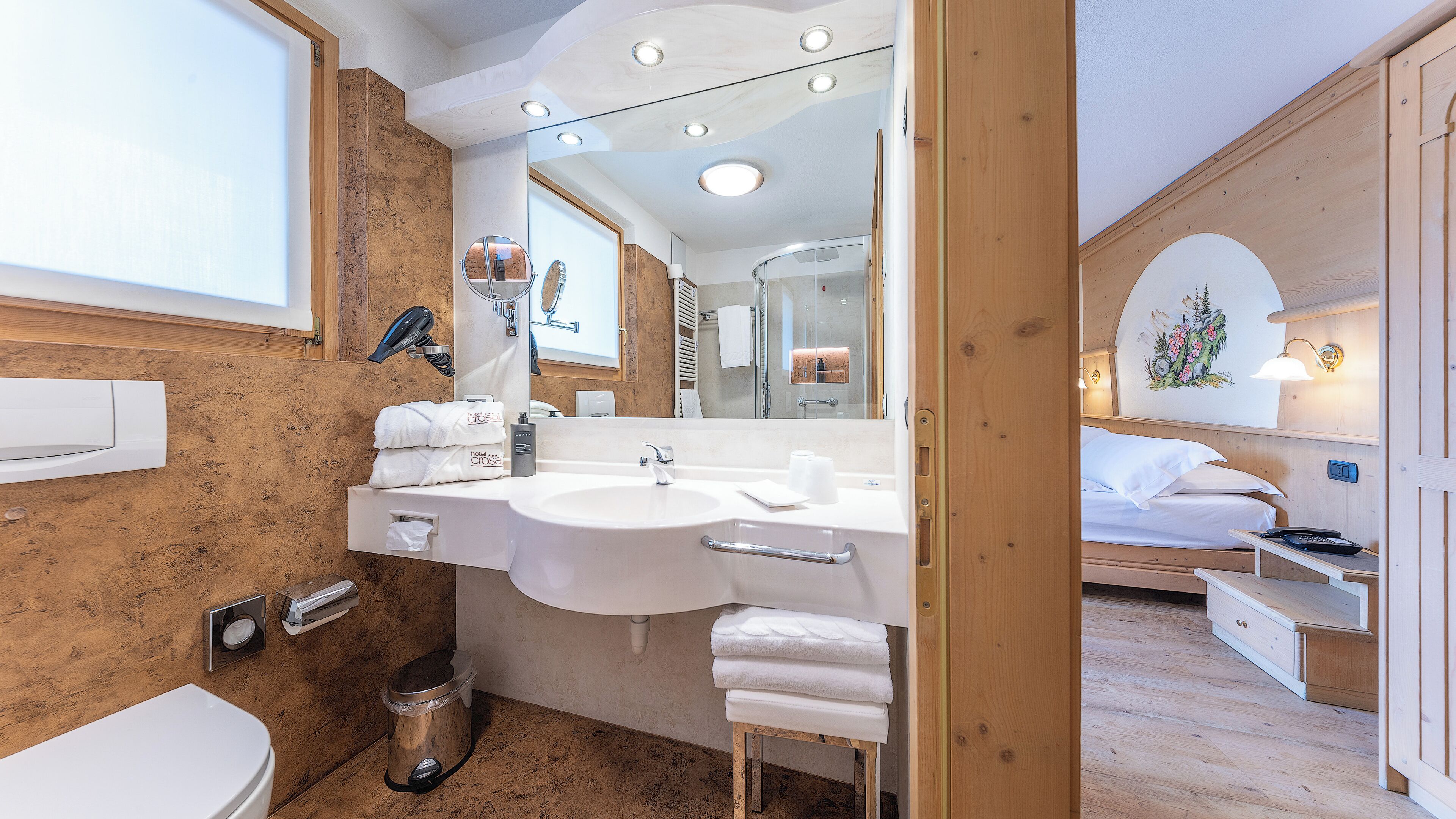 A modern bathroom with a large sink, mirror, and a shower area. There is a toilet and a small trash can.