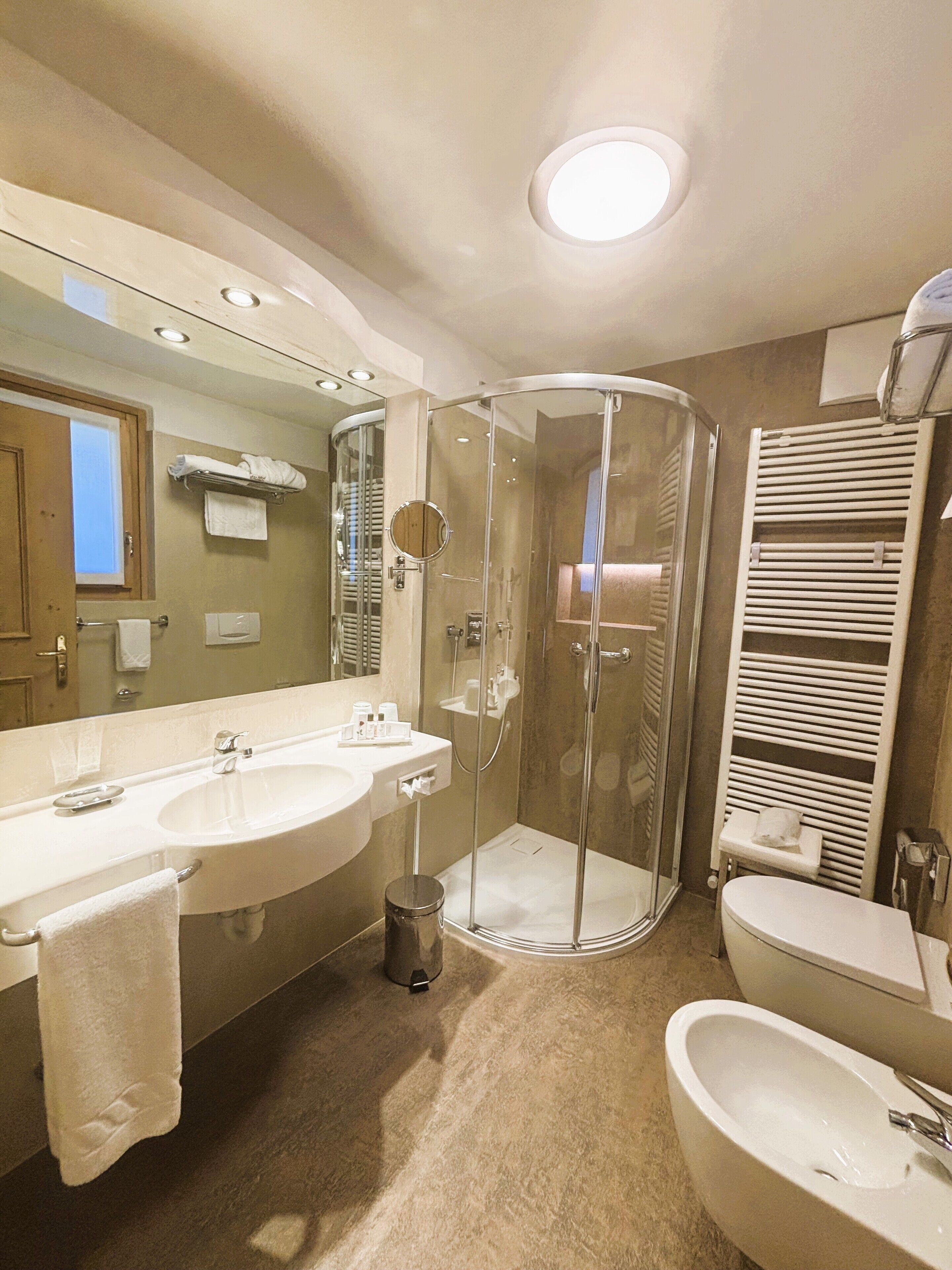A bathroom with a glass-enclosed shower, two sinks, a mirror, and a towel rack.