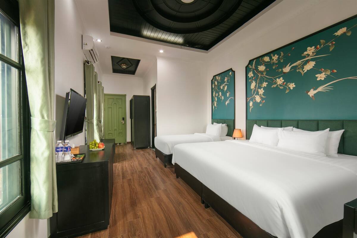 A hotel room with two beds, a TV, a desk with a water bottle, and a green door.