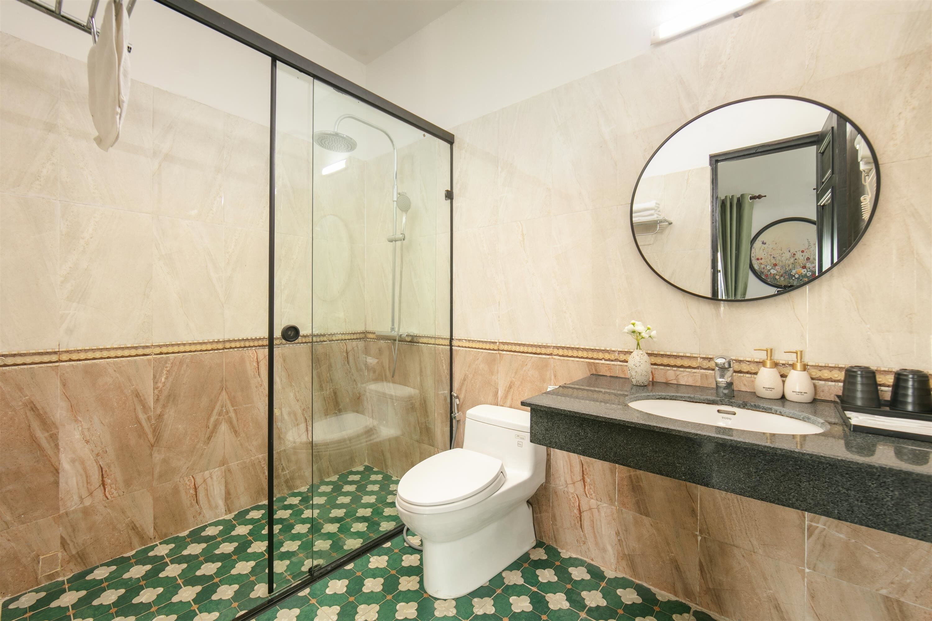 A bathroom with a glass shower enclosure, a toilet, a sink with a mirror, and patterned floor tiles.