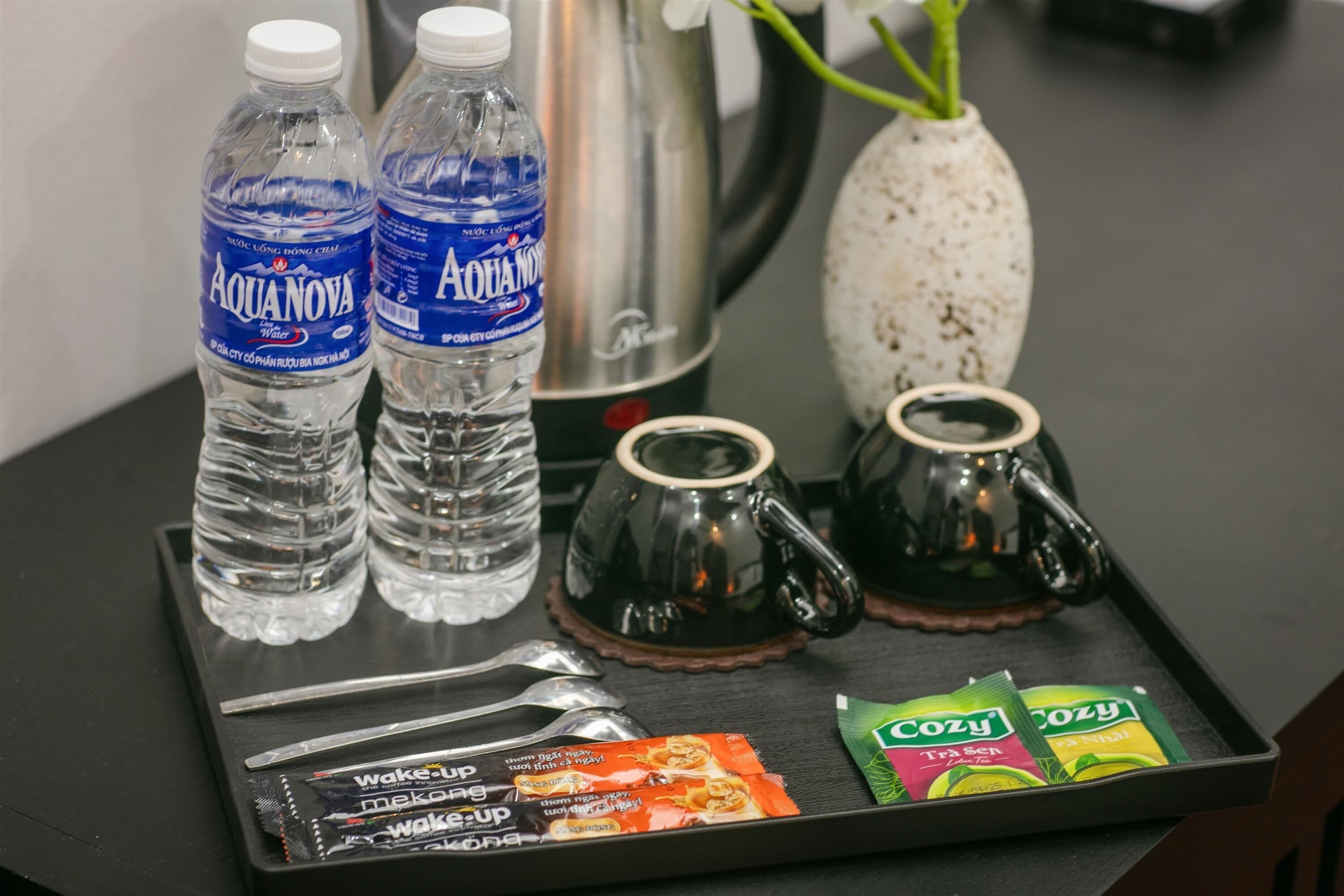 A tray with two bottles of Aquanova water, two teapots, two spoons, and two packets of Cozy tea.