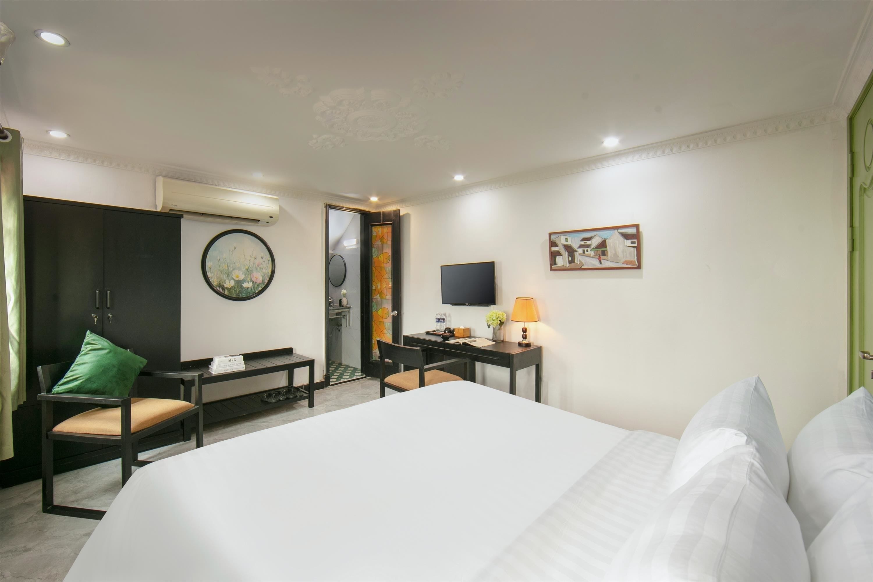 A hotel room with a large bed, a desk with a chair, a television, and a small table with a lamp.