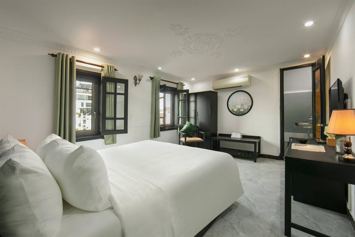 A hotel room with a large bed, a desk, a chair, a mirror, and a window with curtains.