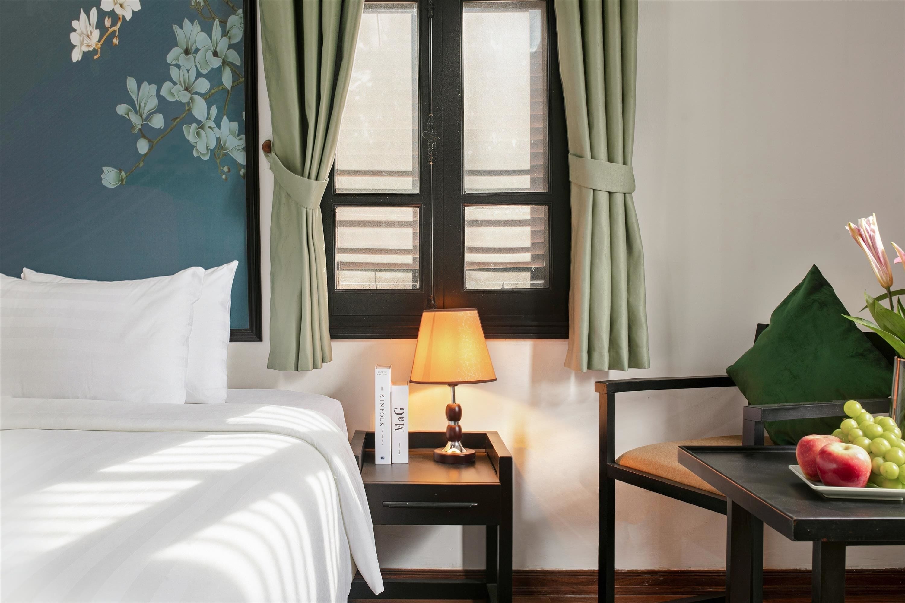 Une chambre d’hôtel avec un lit, une table de chevet avec une lampe, une chaise et une table avec des fruits.