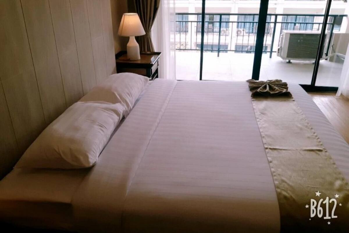 Quarto de hotel com cama, mesa de cabeceira com abajur e vista para a varanda externa.