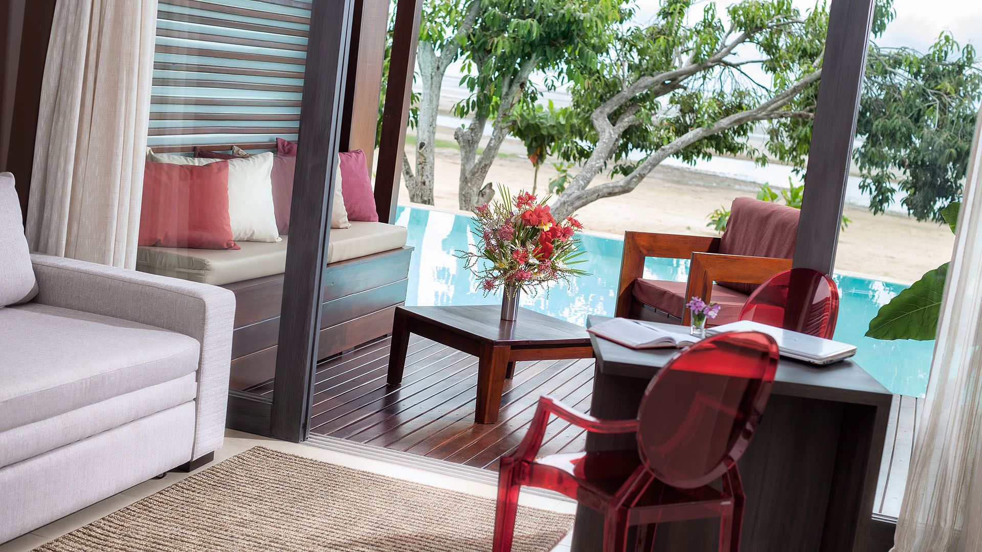Una habitación con sofá, una mesa con un florero y vistas a la playa y árboles.