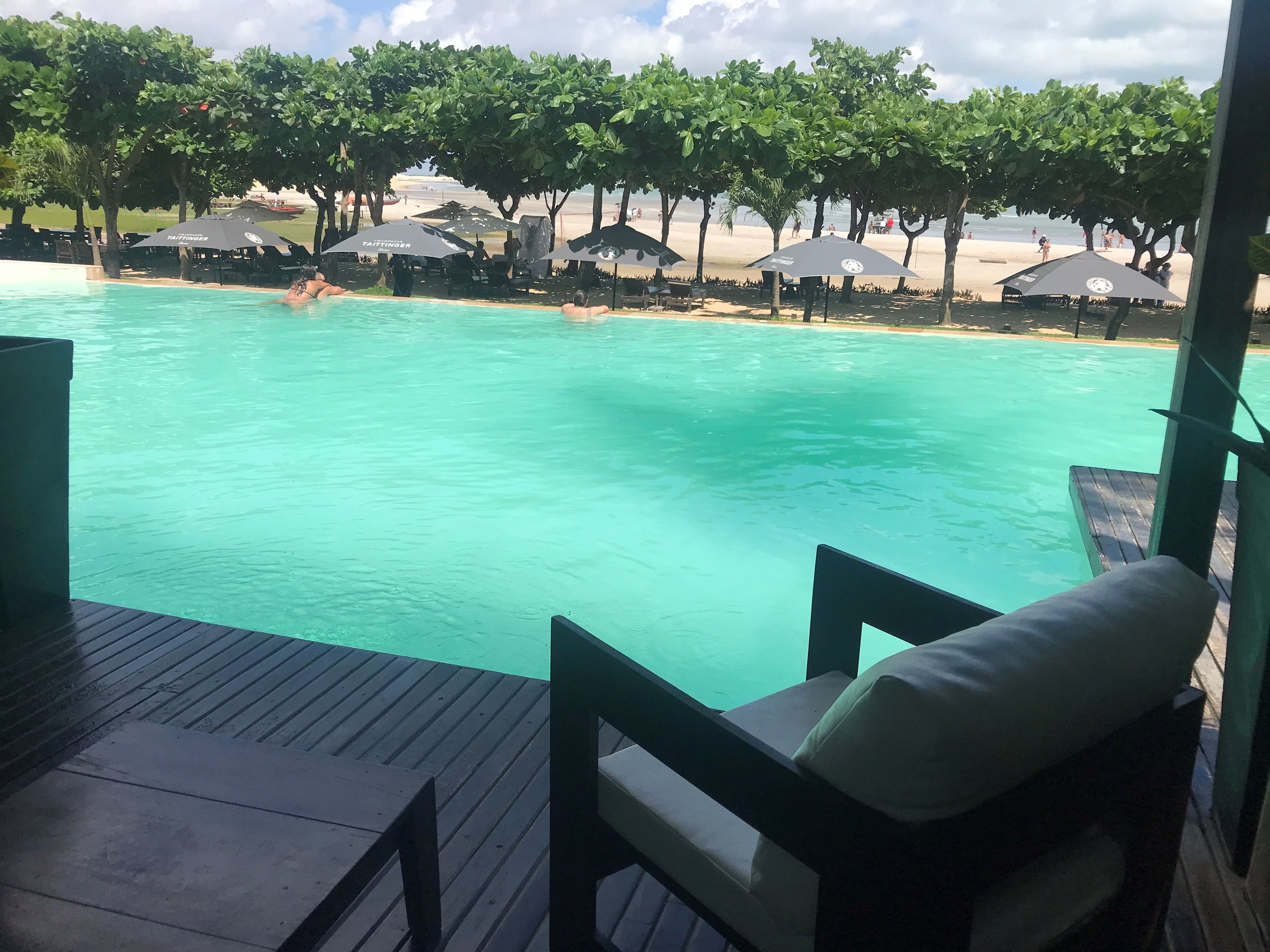 Uma área de piscina com vista para a praia, cercada por guarda-sóis e espreguiçadeiras.