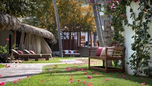 A garden area with a thatched-roof hut, a wooden bench, and a bed with pillows. - Essenza Hotel (Jijoca de Jericoacoara)