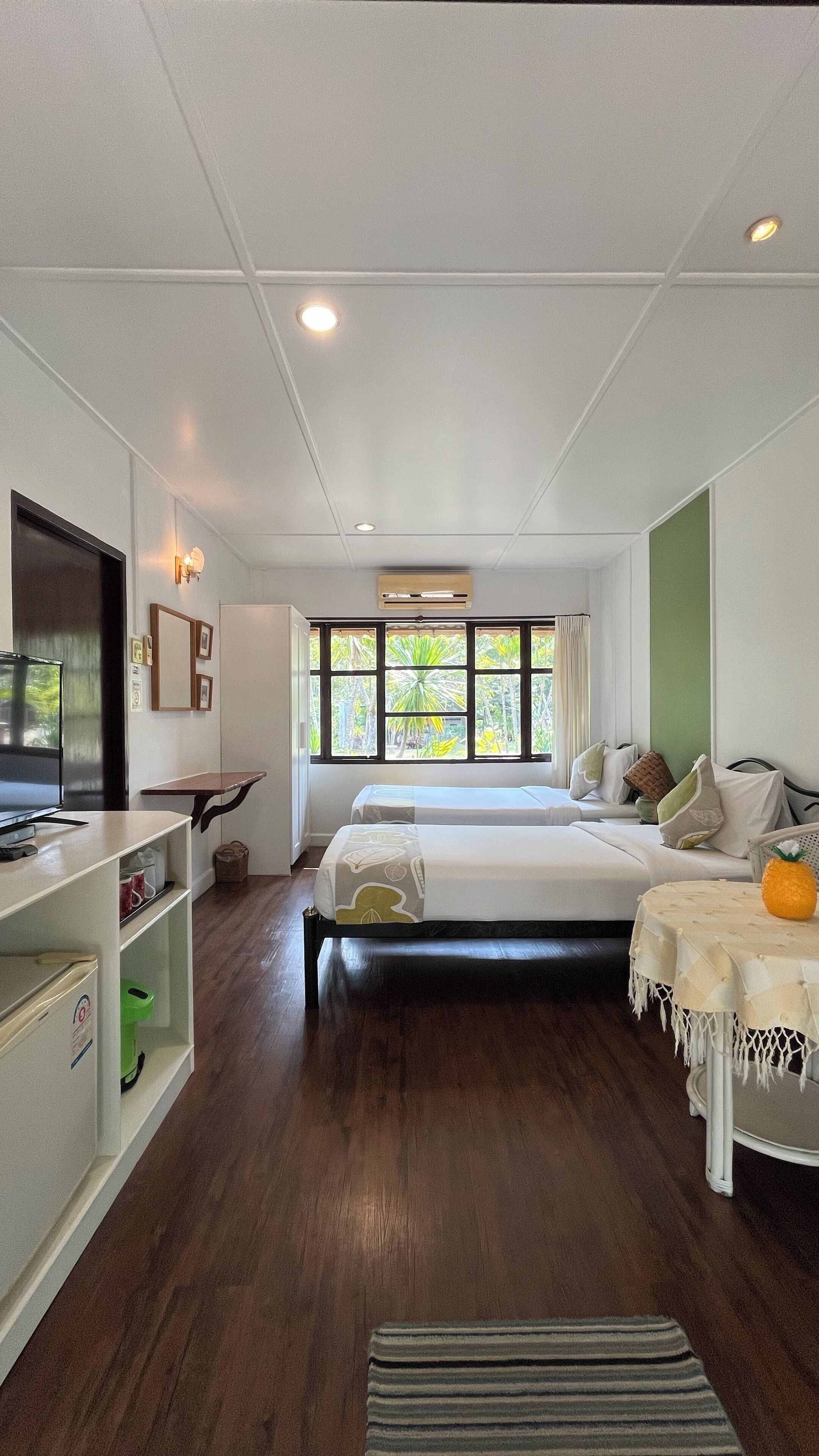 A modern hotel room with a large bed, a desk, a TV, and a window with a view of greenery.