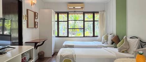 A modern hotel room with a large bed, a desk, a TV, and a window with a view of greenery.